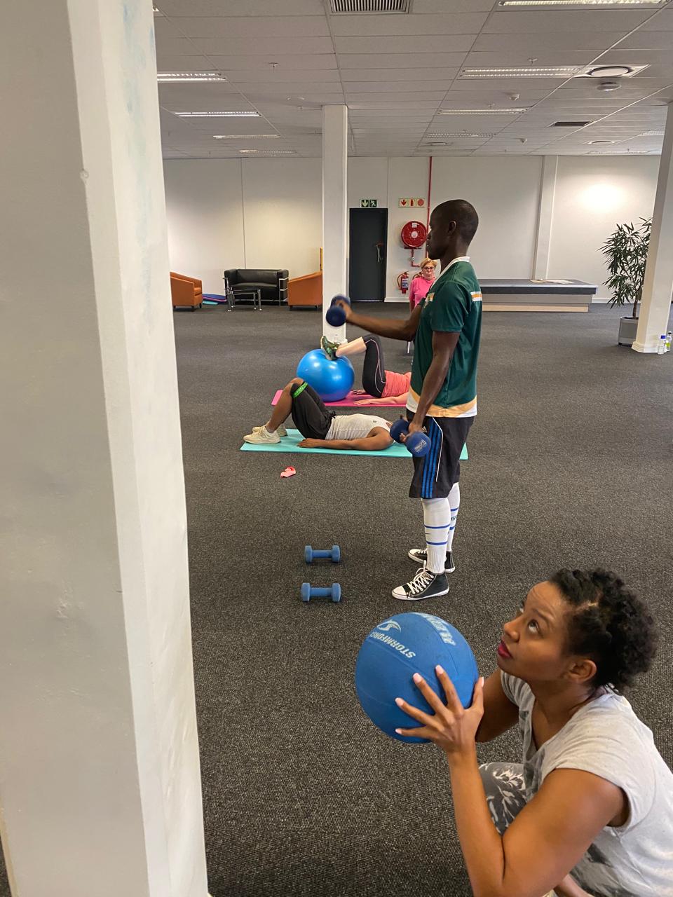 Trainer coaching employees through a dumbbell workout in their office